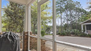 A covered patio with a grill, a brick wall, and a view of a street and trees. - Longleaf Pines by AvantStay | Community Pool (Santa Rosa Beach)
