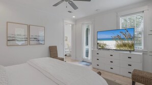 A bedroom with a bed, a ceiling fan, a TV on a dresser, and a door leading to a bathroom. - Longleaf Pines by AvantStay | Community Pool (Santa Rosa Beach)