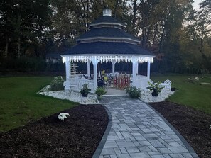 A gazebo with a white exterior and a tiled pathway leading to it.