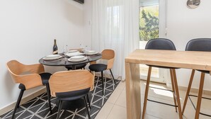 A dining area with a round table set for four, surrounded by wooden chairs with black cushions. A bottle of wine and glasses are on the table. - 1 bedroom nice apartment in Pula (Pula)