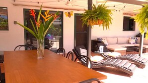 A wooden table with chairs, a vase with flowers, and a seating area with lounge chairs and a sofa. - Ultimate heaven of comfort and relaxation. Entire house, large private pool.  (Kewarra Beach)
