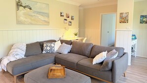 A living room with a sectional sofa, a wooden side table, and a painting on the wall. - Ultimate heaven of comfort and relaxation. Entire house, large private pool.  (Kewarra Beach)