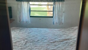 A bedroom with a bed, a window with curtains, and decorative wall panels. - Russell's Roost Camping , Boating, Fishing ON Martiny Chain of Lakes. (Barryton)