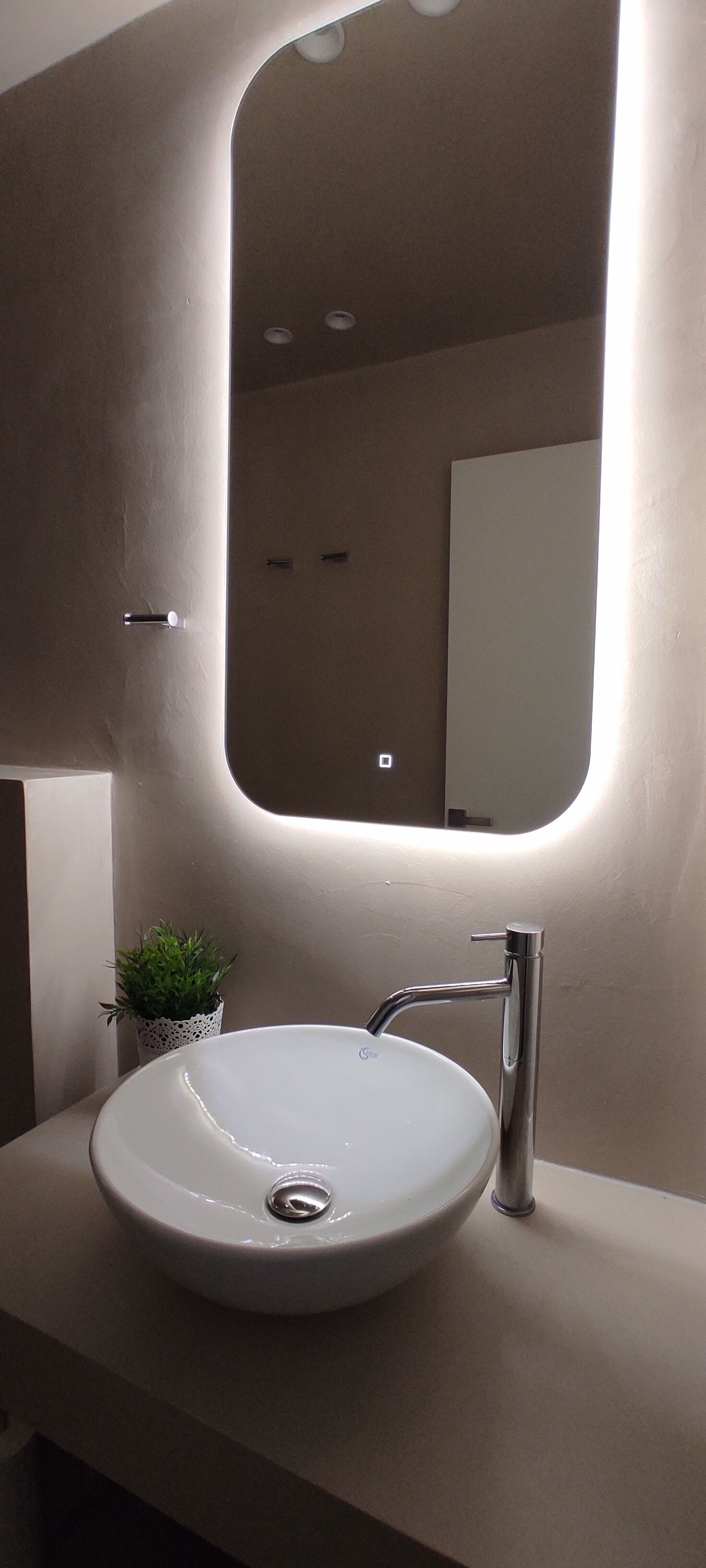 Ein modernes Badezimmer mit einem weißen Waschbecken, einem Spiegel und einer kleinen Topfpflanze.