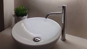 Ein modernes Badezimmer mit einem weißen Waschbecken, einem Spiegel und einer kleinen Topfpflanze.