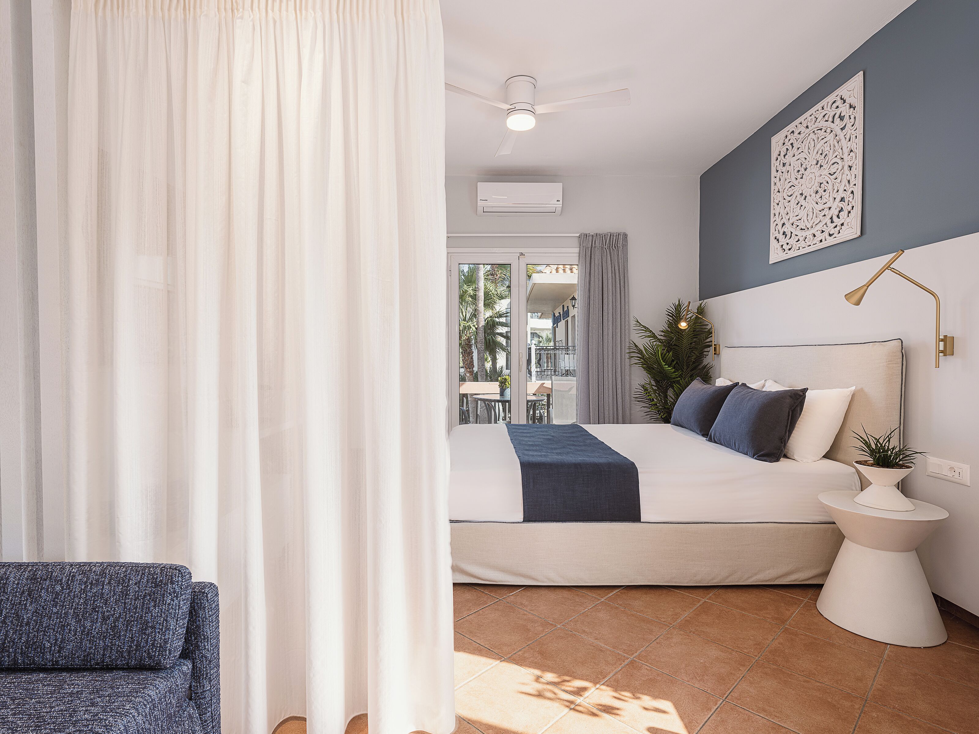 A modern bedroom with a large bed, a bedside table, a floor lamp, and a view of the outside balcony.