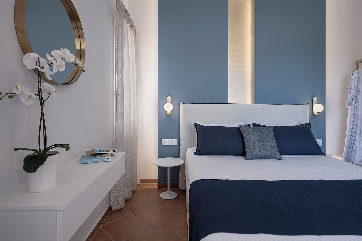 A bedroom with a bed, a bedside table, a mirror, and a wall-mounted light fixture.