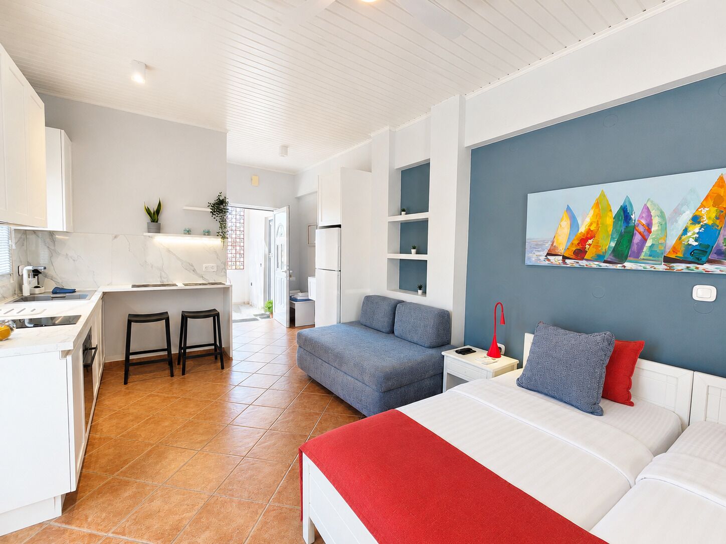 A modern room with a bed, a desk, a chair, and a sofa. There is a painting on the wall and a plant on the desk.
