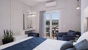 A modern hotel room with a bed, a seating area with a view, a balcony, and a large window. - Elena SeaFront Luxury Apartments (Apokoronas)