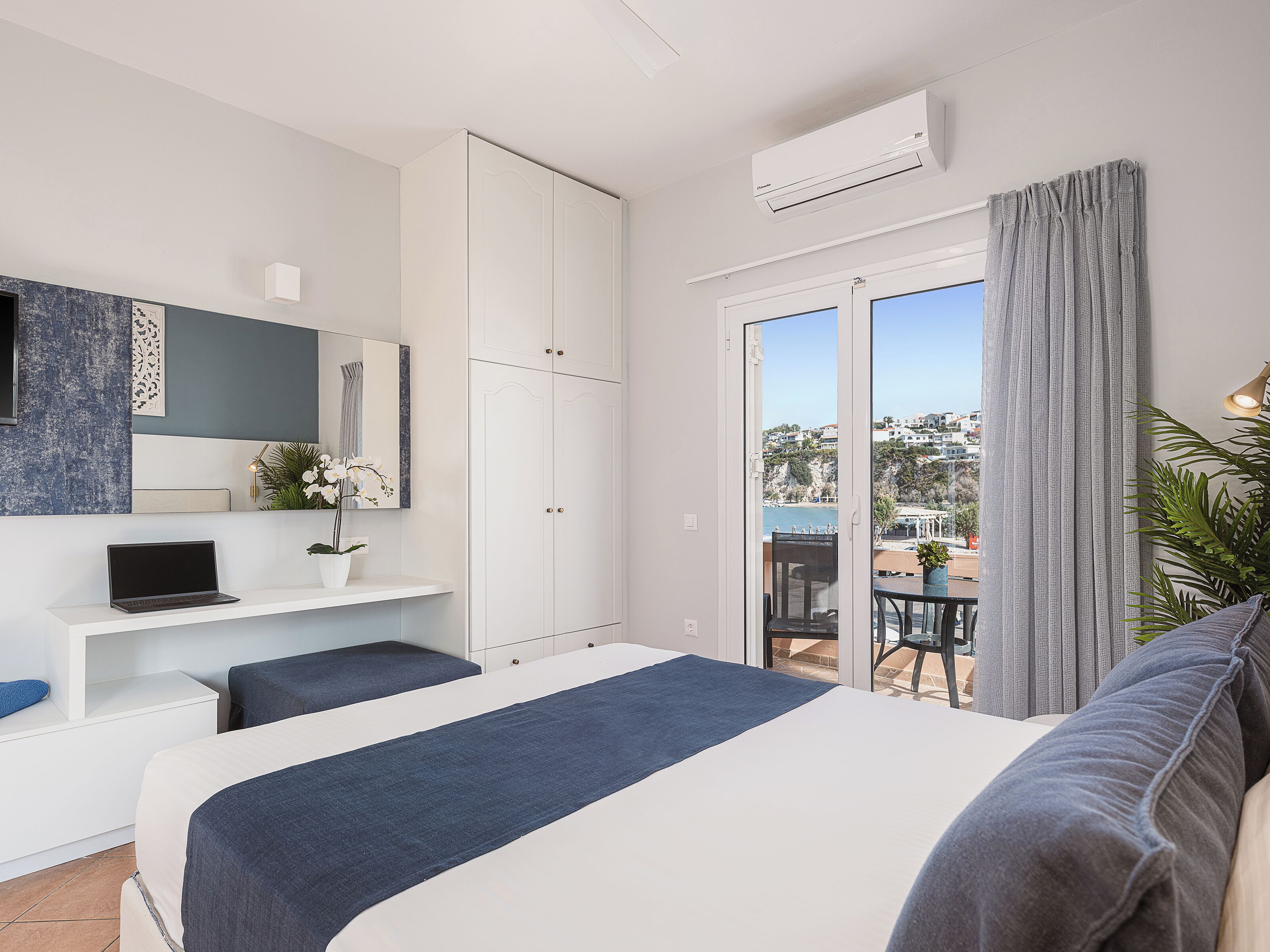 Un dormitorio moderno con cama, escritorio, silla, televisor y balcón con vista al mar.