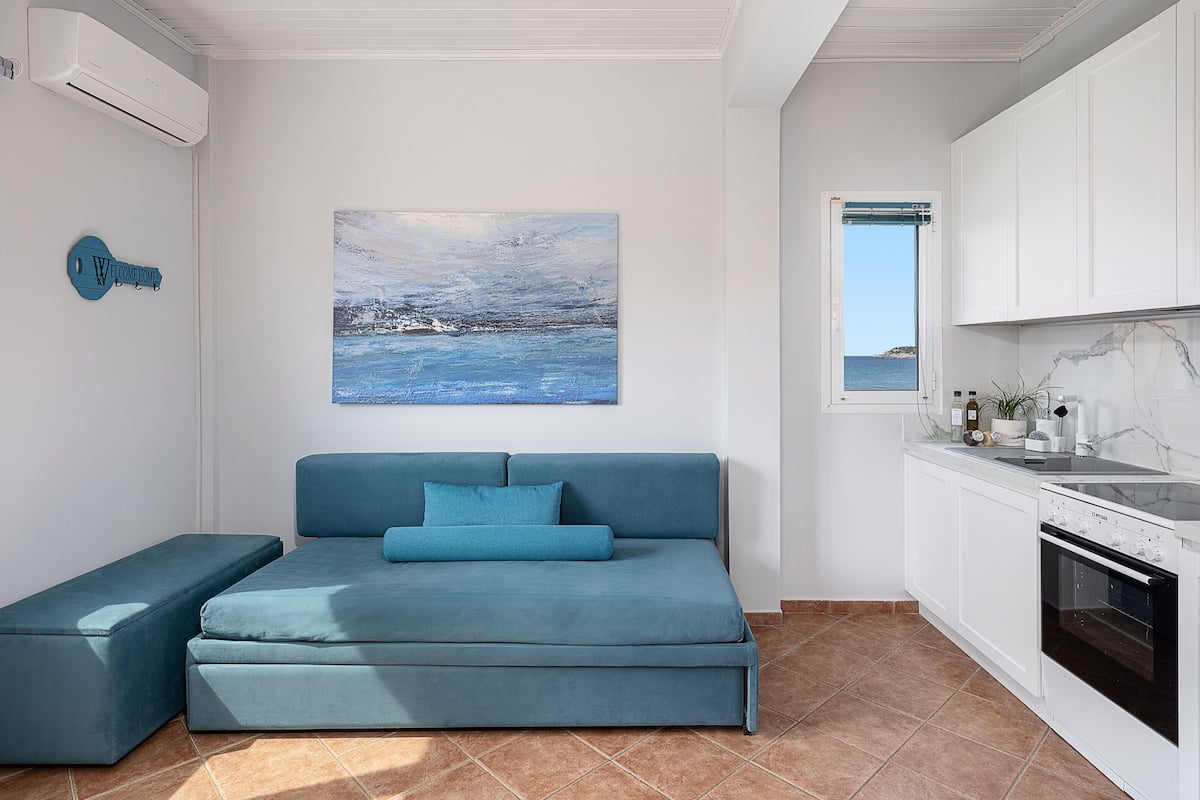 A modern kitchen with white cabinets, a built-in oven, and a window with a view of the sea.