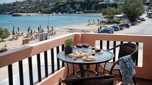 A balcony with a table set for two, overlooking a beach and a coastal town. - Elena SeaFront Luxury Apartments (Apokoronas)