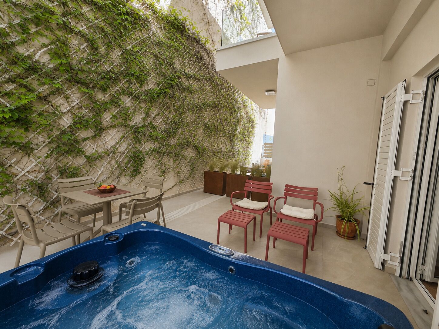 A hot tub, outdoor seating, and a wall covered with climbing plants.