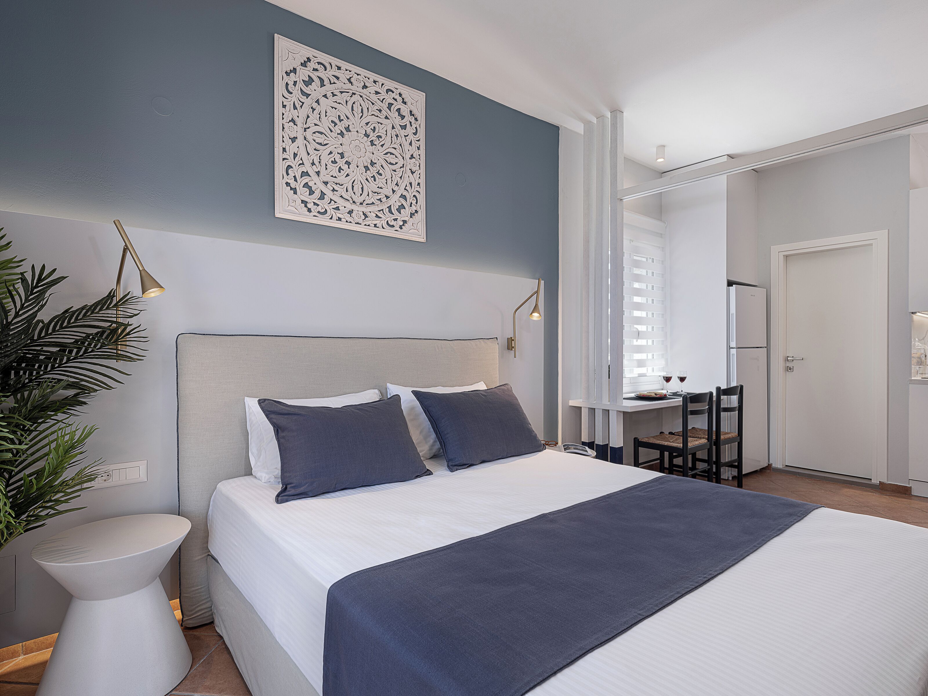 Un dormitorio moderno con cama, mesitas de noche, una planta en maceta y un adorno en la pared.