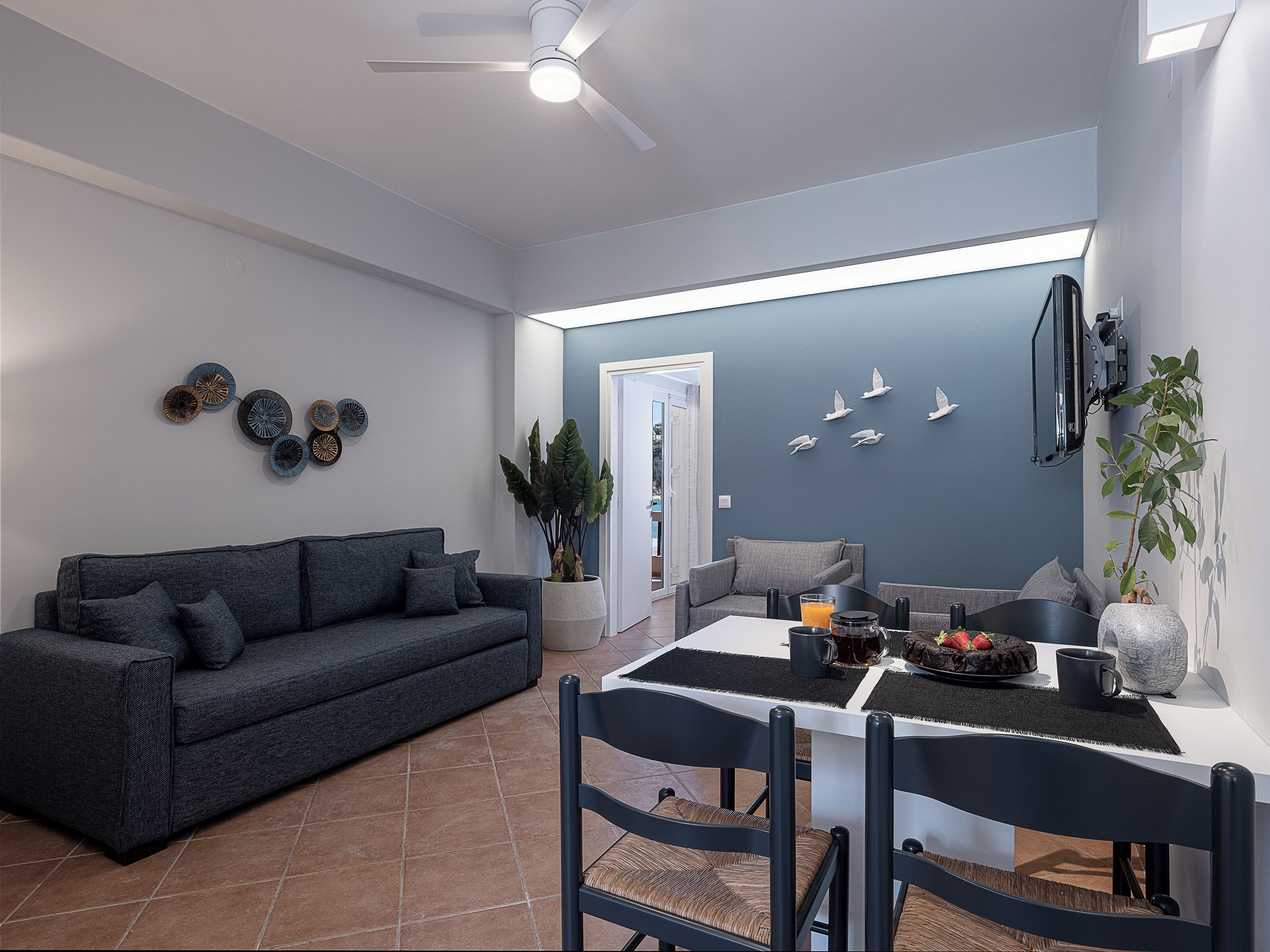 A modern living room with a dark grey sofa, a dining table with chairs, and decorative wall art.