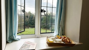 Ett brickbord med frukost placerat på en fönsterbräda, med en tidning, ett croissant och ett glas apelsinjuice.