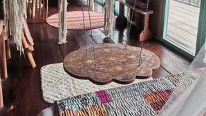 A room with a hammock, macramé hanging, and a large woven rug.