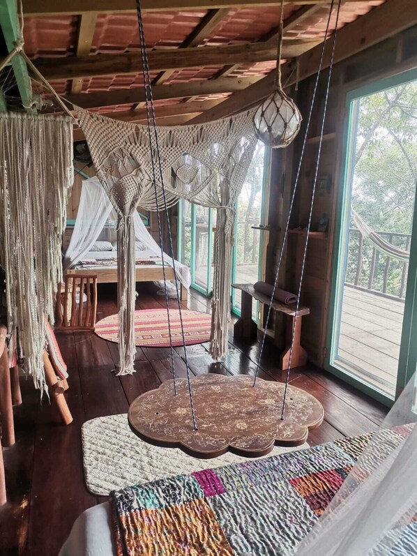 A room with a hammock, macramé hanging, and a large woven rug.