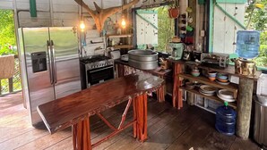 A rustic kitchen with a large wooden table, hanging antlers, and a view of greenery outside.