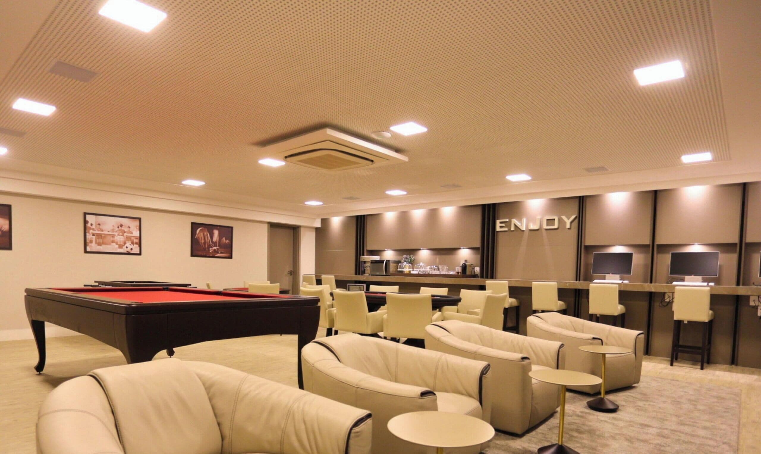 A room with a pool table, comfortable seating, a bar area, and a ceiling with recessed lighting.