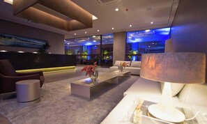 Eine moderne Hotelhalle mit einer Couch, einem Couchtisch mit Blumenvase, einer Lampe und einer Rezeption.