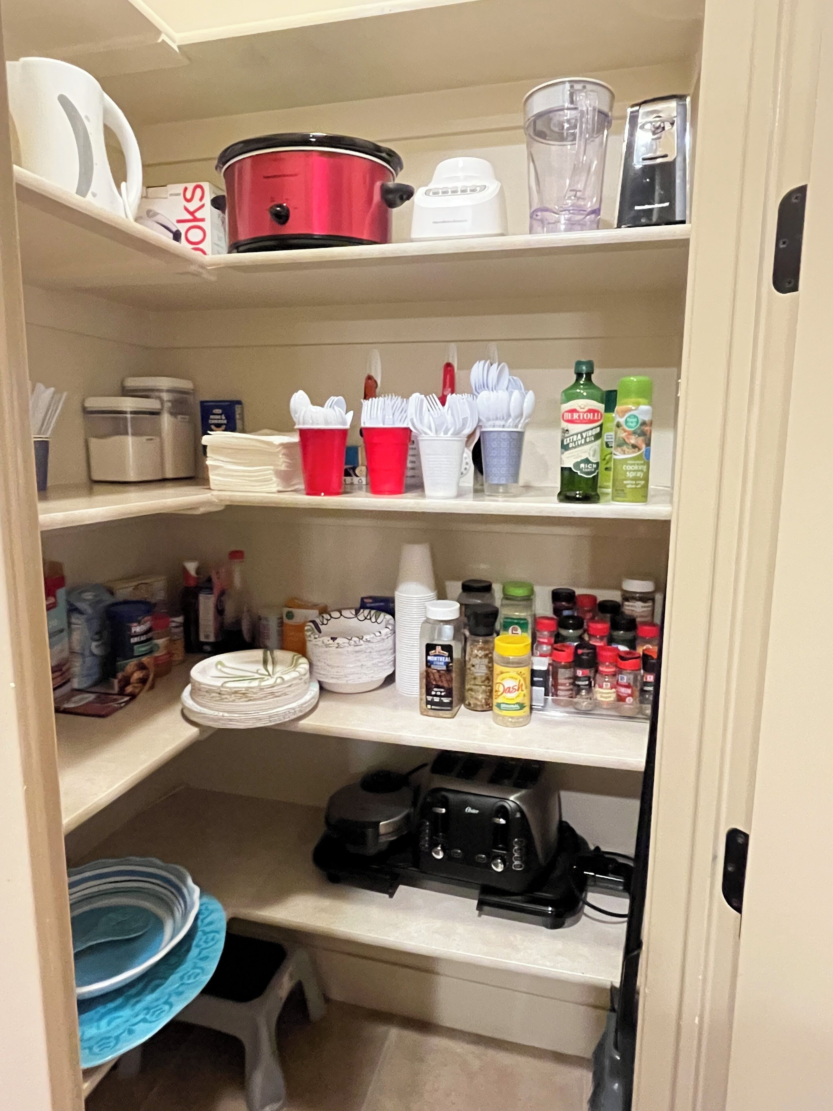 A kitchen pantry with shelves containing various kitchen items, including a red slow cooker, a white blender, and several spice bottles.