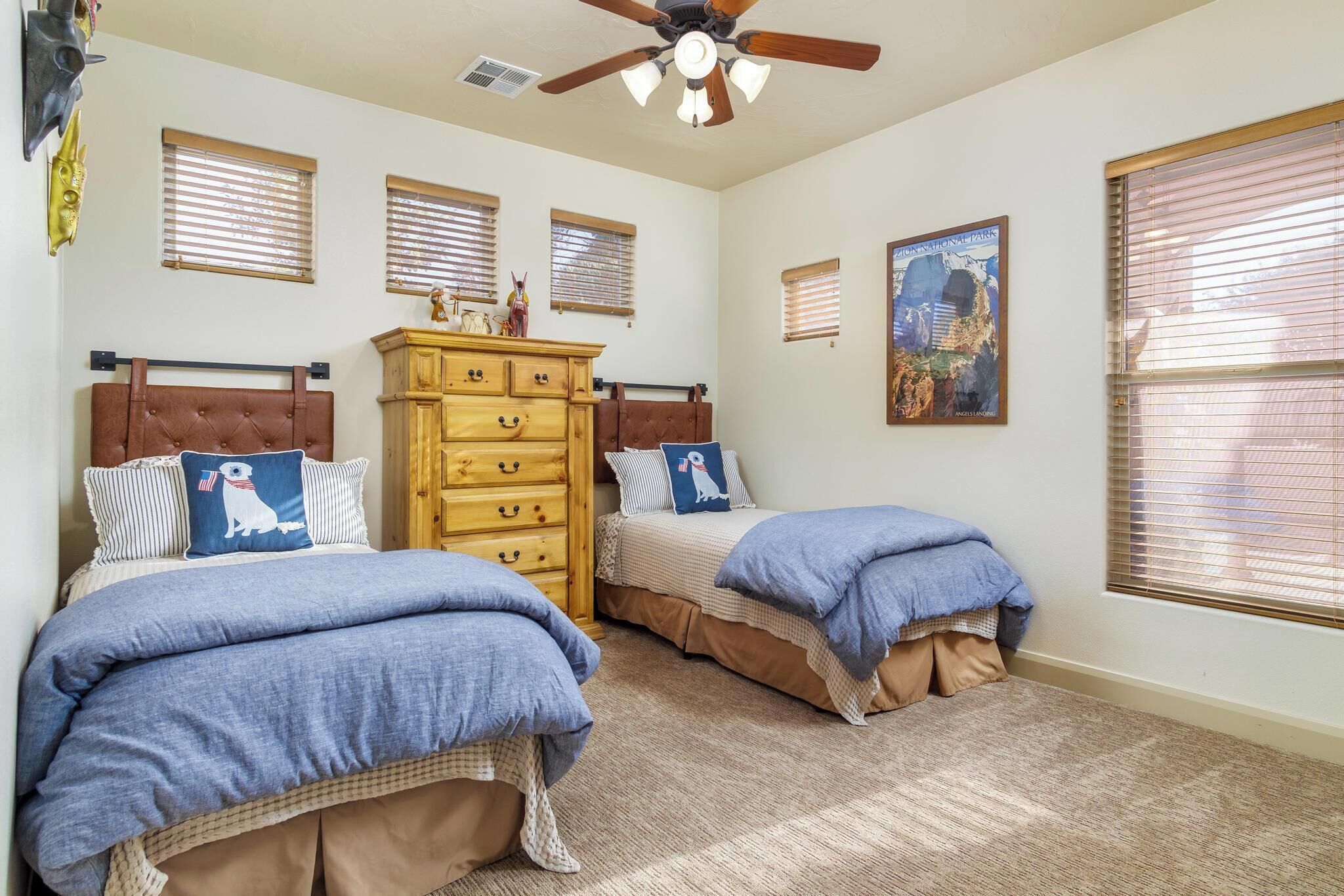 A bedroom with two beds, a wooden dresser, and a ceiling fan.