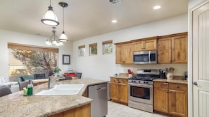 A modern kitchen with granite countertops, wooden cabinets, stainless steel appliances, and a large window providing natural light.