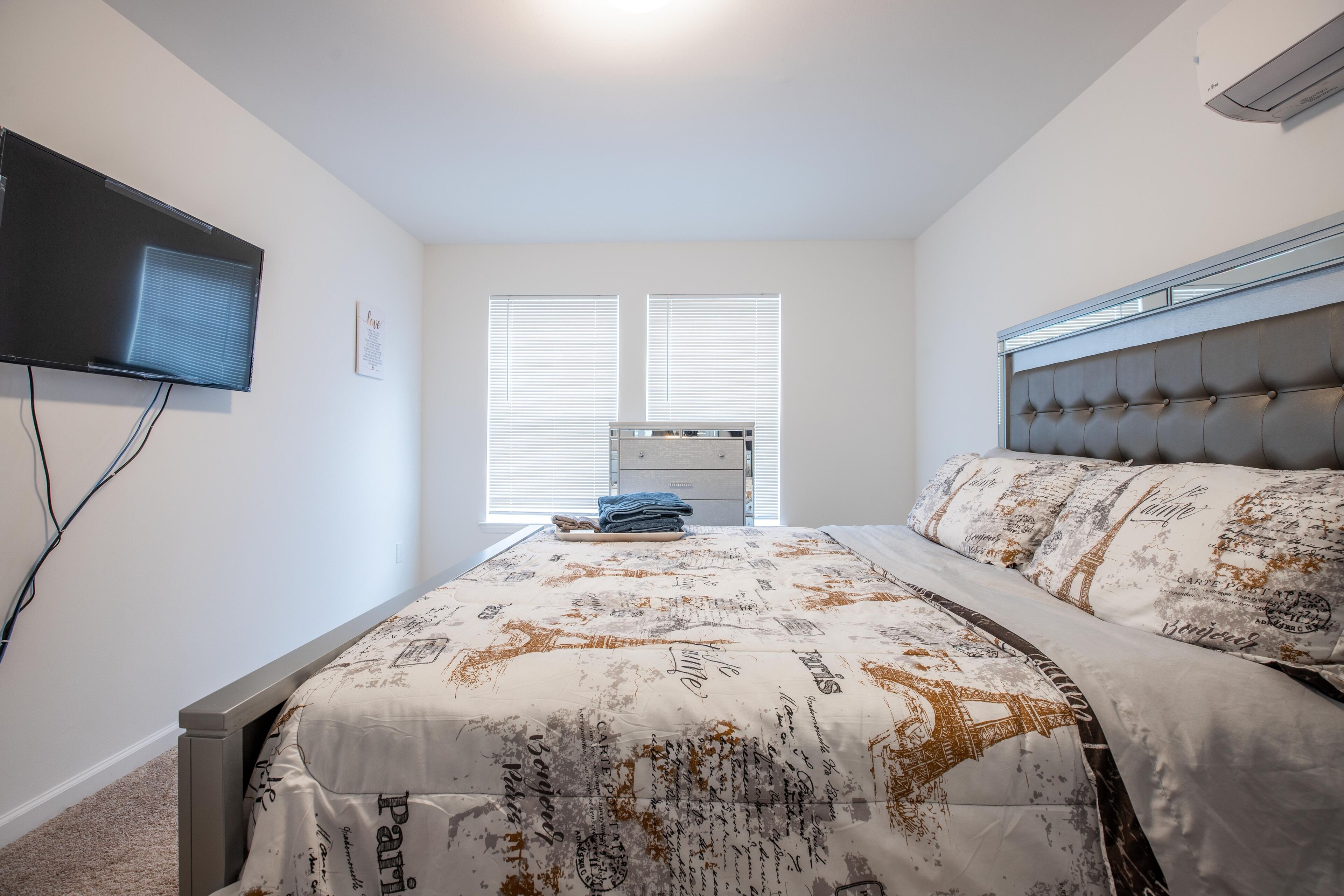 A bedroom with a bed, a television, and a window with blinds.