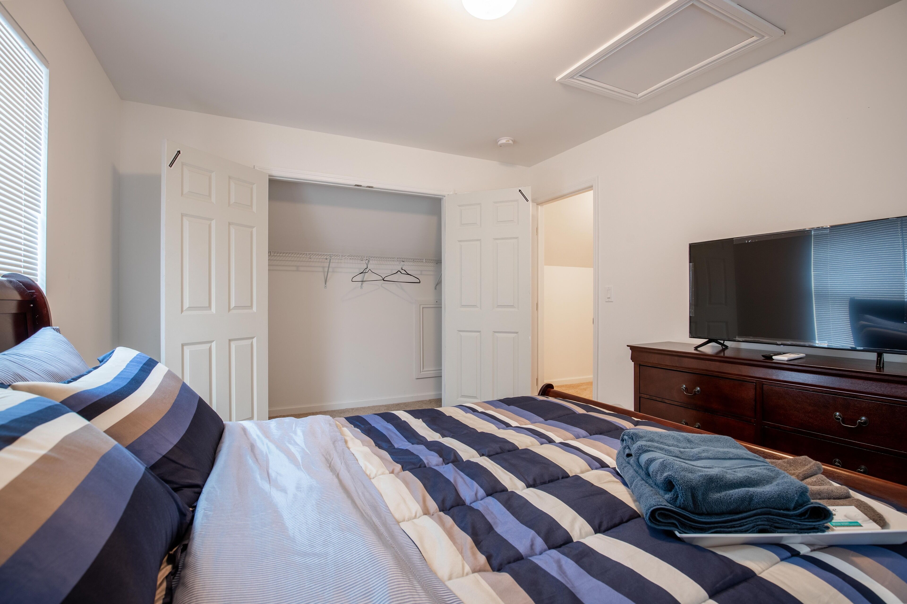 Een slaapkamer met een bed, een dressoir, een televisie en een inloopkast.