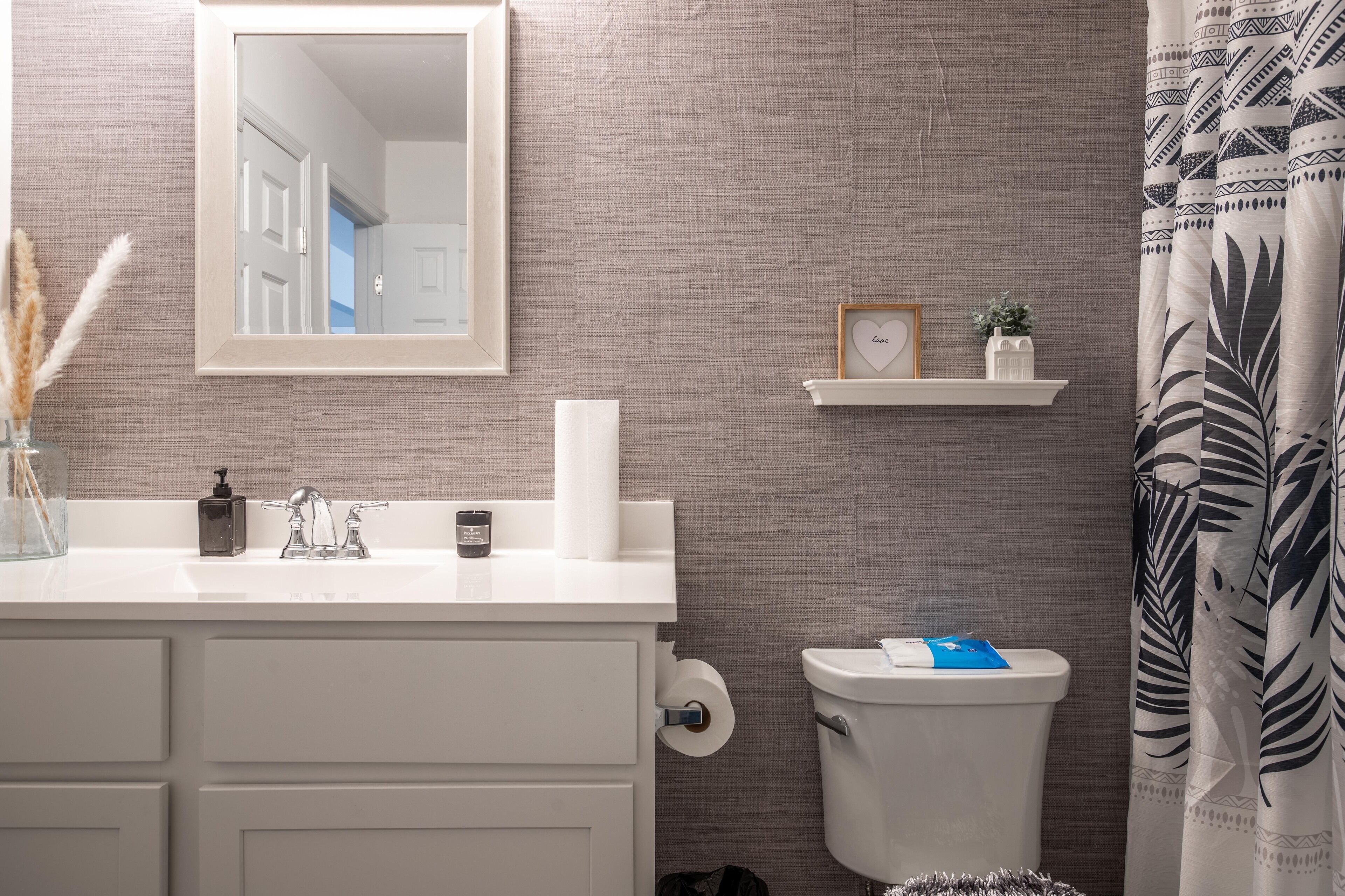 A bathroom with a white vanity, a mirror, a toilet, and a shower curtain.