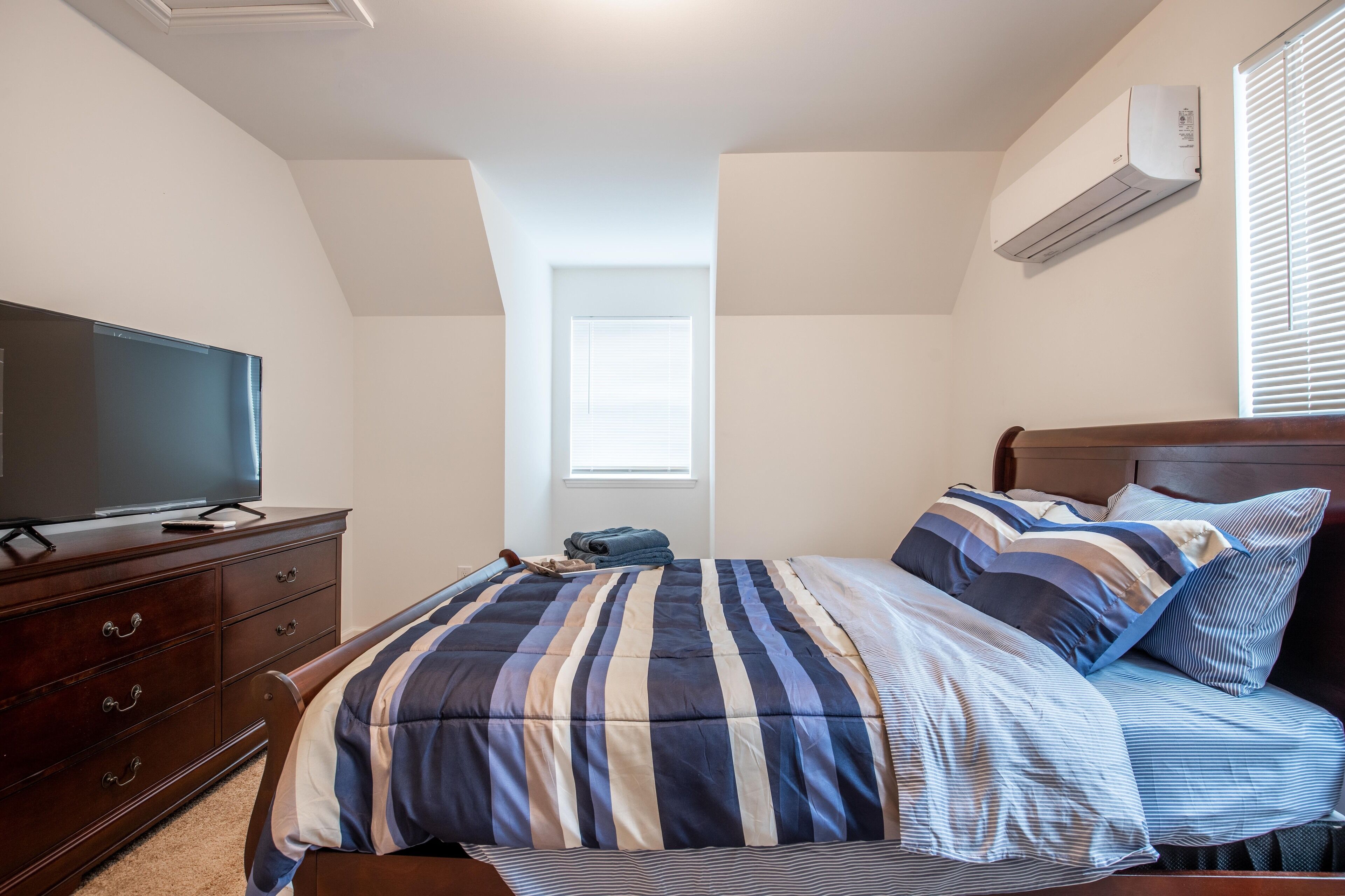 A bedroom with a bed, a dresser, a television, and an air conditioning unit.