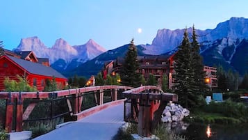 A wooden bridge over a river, surrounded by buildings with red roofs and a mountain backdrop.