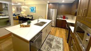 A modern kitchen with a central island, stainless steel appliances, and a dining area with a sofa and table. - Luxury, Spacious, New, Entire Condo Suite, Scenery Year-round Mountain Getaway (Canmore)