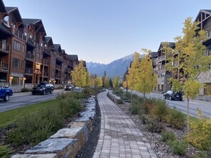 Un hotel de diverses plantes amb balcons, un passeig pavimentat i un paisatge de muntanya al fons.