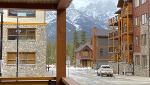 A building with stone and wood exterior, wooden balconies, and a view of snow-capped mountains. - Luxury, Spacious, New, Entire Condo Suite, Scenery Year-round Mountain Getaway (Canmore)