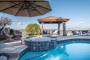 Une piscine avec un jacuzzi, du mobilier d’extérieur et une pergola.