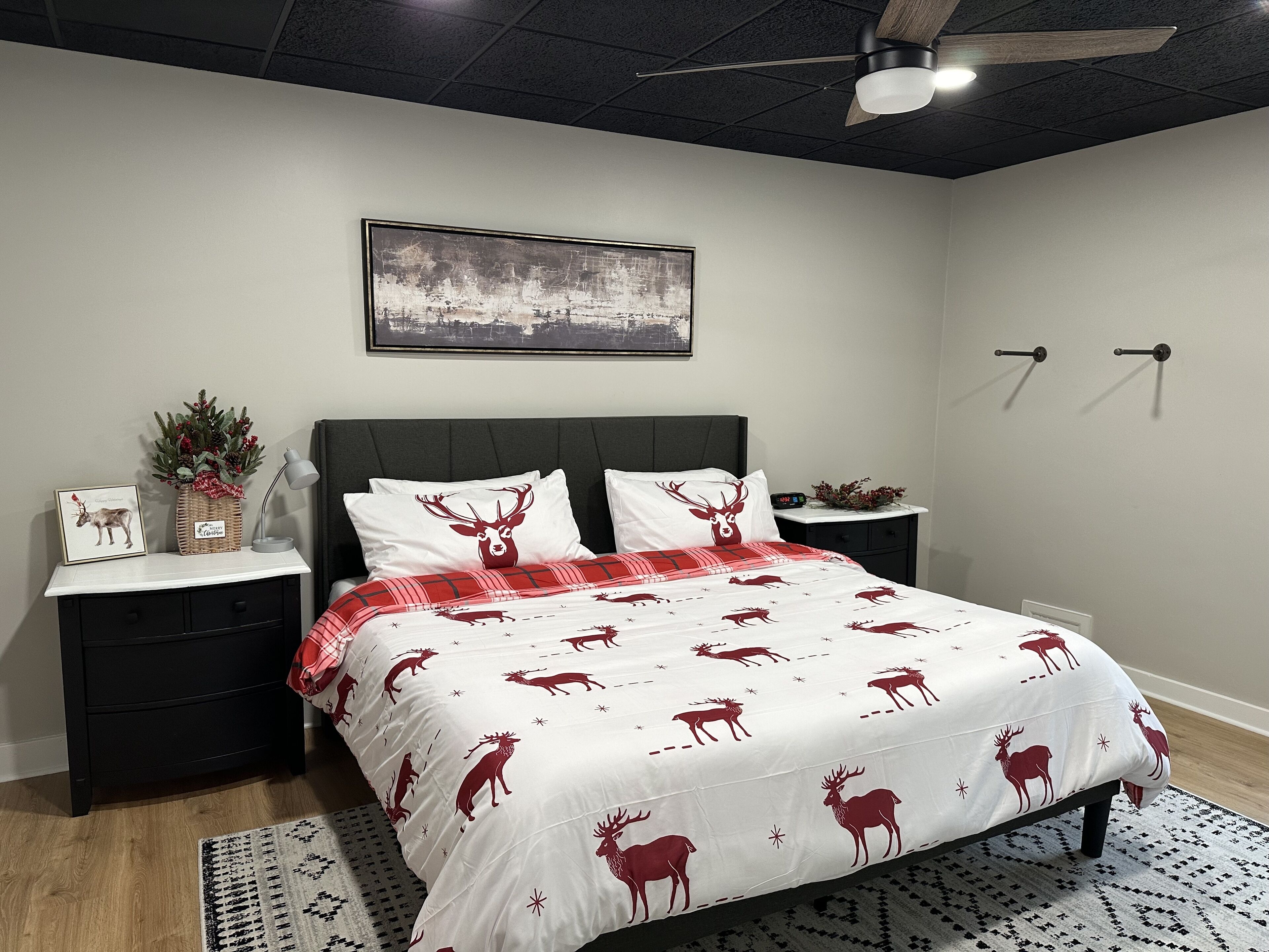 Ein Schlafzimmer mit einem Bett, Nachttischen, einer Wanduhr, einem Deckenventilator und einem gerahmten Bild an der Wand.