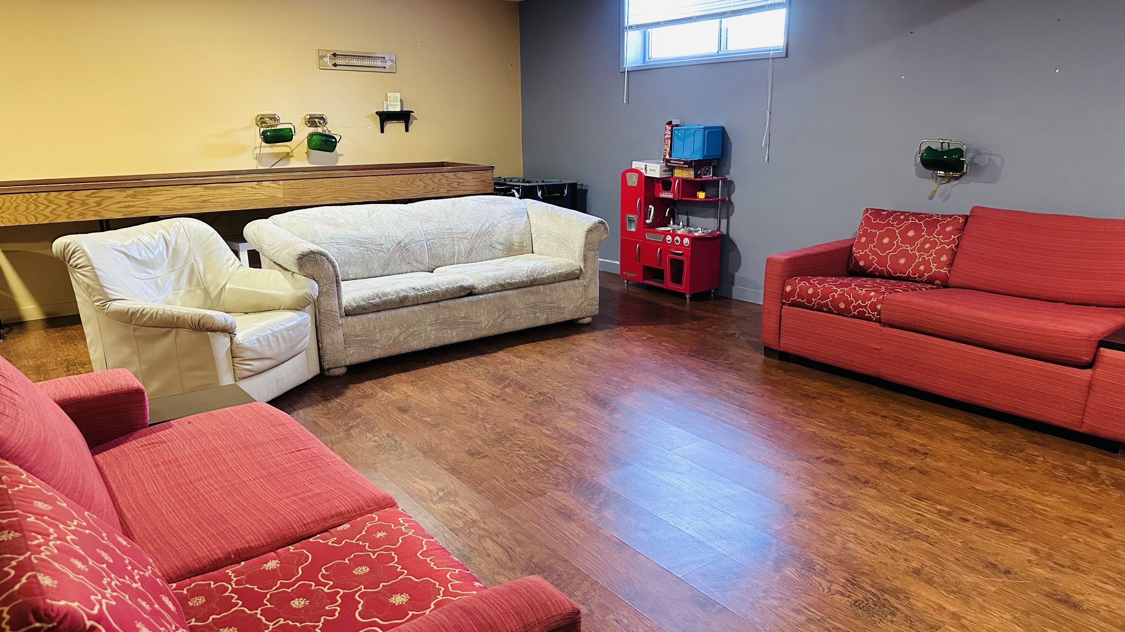 Ein Wohnzimmer mit einem beigefarbenen Sofa, einem roten Sofa und einem weißen Sofa. In der Mitte steht ein Couchtisch aus Holz.