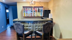 Eine Bar mit zwei Ledersesseln, einer Flaschenregal und einem schwarzen Kühlschrank.