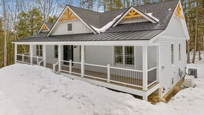 Uma cabana branca com varanda e telhado em forma de galeria, rodeada por neve e árvores.