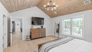 Quarto com cama grande, teto de madeira e televisão em uma cômoda.
