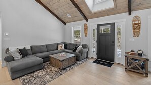 Uma sala de estar moderna com um sofá seccional cinza, uma mesa de centro de madeira e uma porta preta.