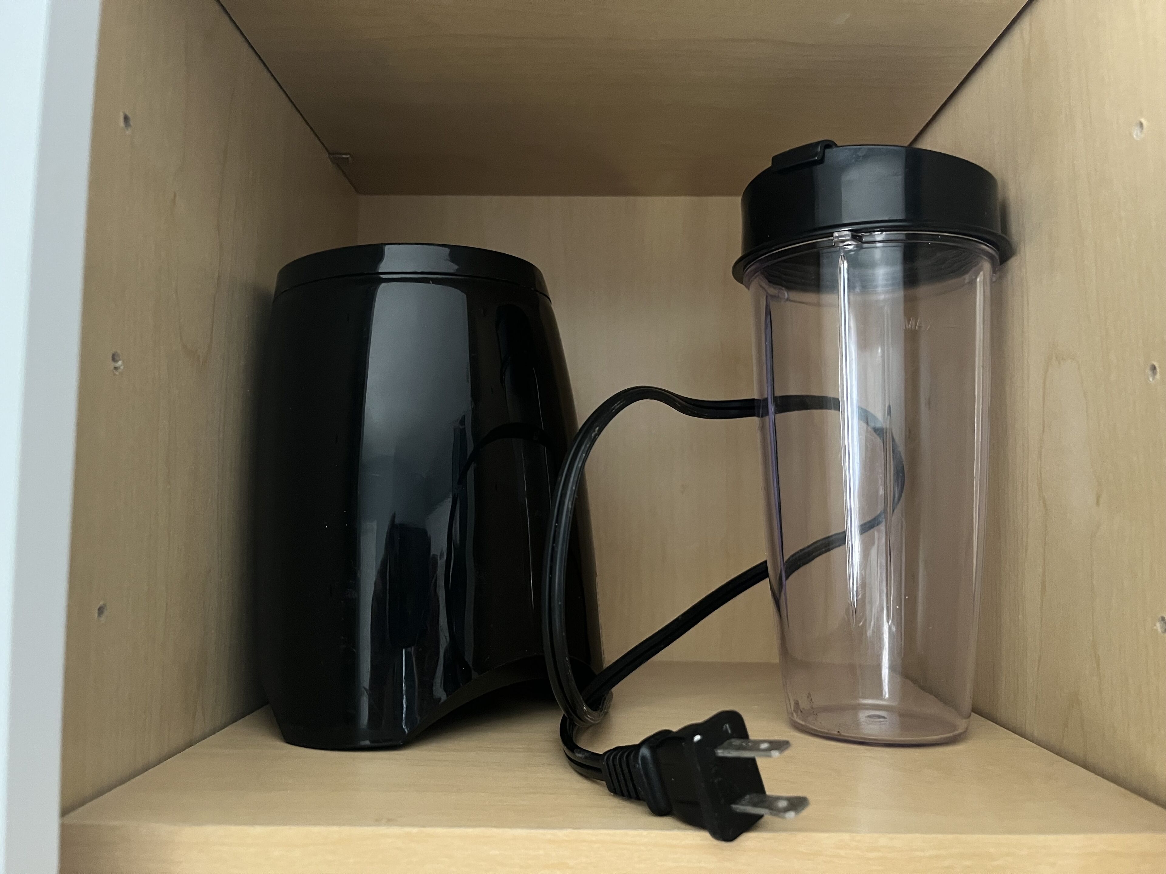 A wooden shelf with a black electric kettle and a clear thermos.
