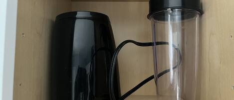 A wooden shelf with a black electric kettle and a clear thermos.