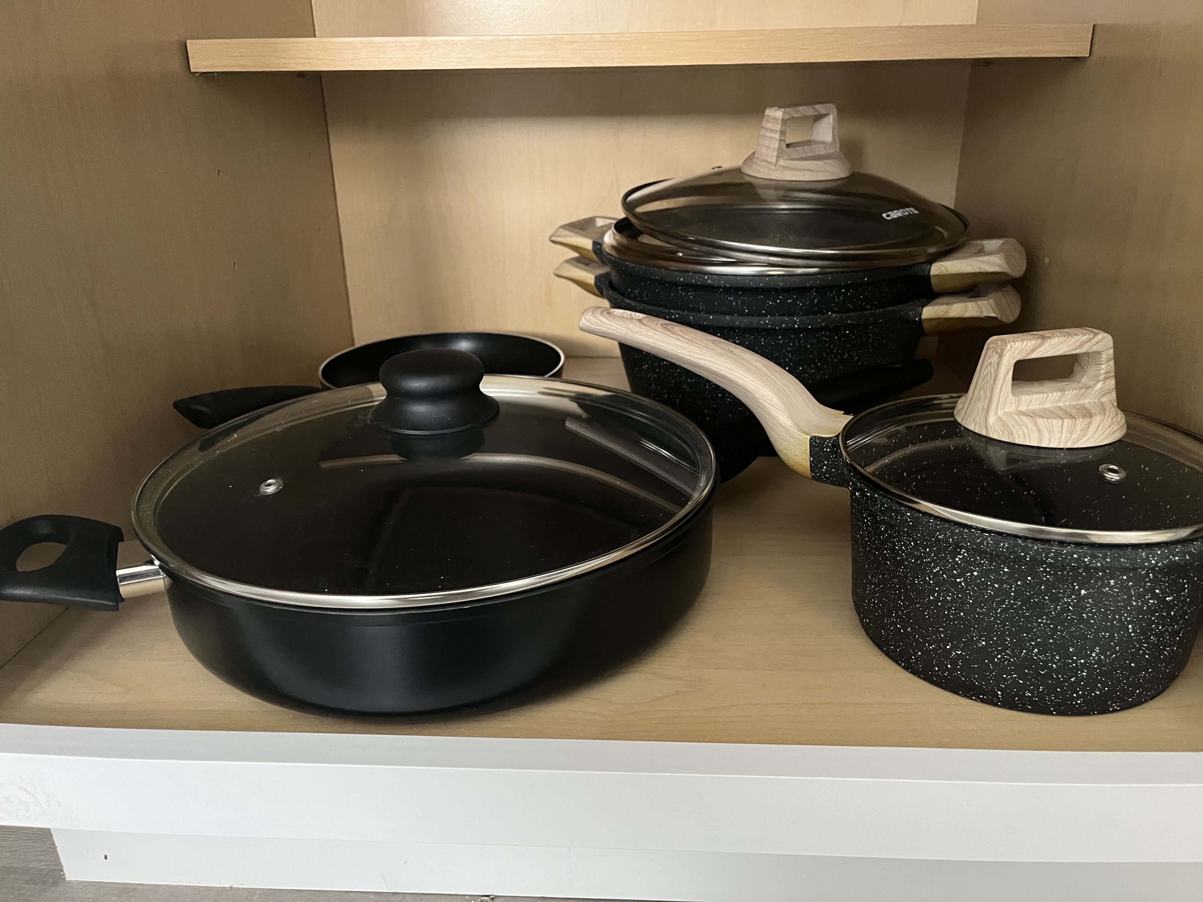 Cuina amb taulell de fusta, una olla negra amb tapa, una paella negra amb tapa i una cassola negra amb tapa.