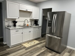 A modern kitchen with white cabinets, a stainless steel refrigerator, and a granite countertop.