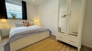 A bedroom with a bed, bedside lamps, a wardrobe, and a window with curtains. - Ferienwohnung für bis zu 6 Personen mit Wunderschöner Luxuriöser Ausstattung - Watt´n Traum (Cuxhaven)