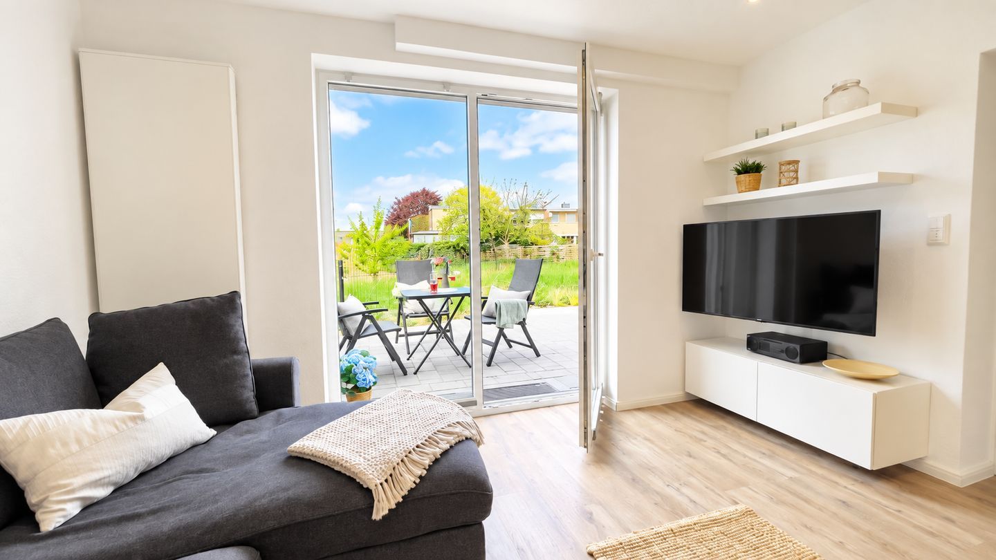 Ein modernes Wohnzimmer mit einer Couch, einem Flachbildfernseher und einer Schiebetür zu einer Terrasse.