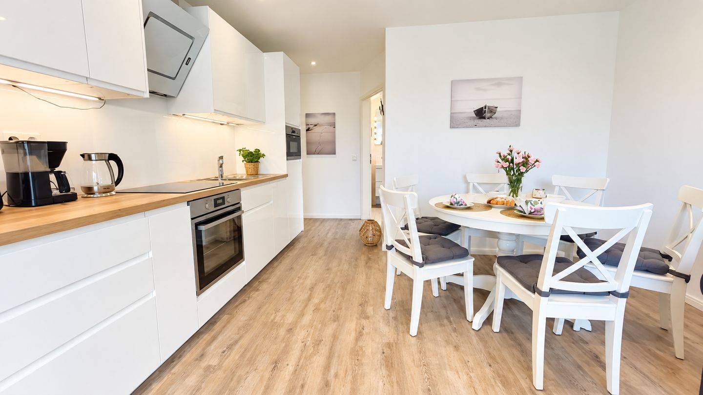 Eine moderne Küche mit weißen Schränken, einer Holz Arbeitsplatte und einem Essbereich mit weißen Stühlen und einem Tisch.